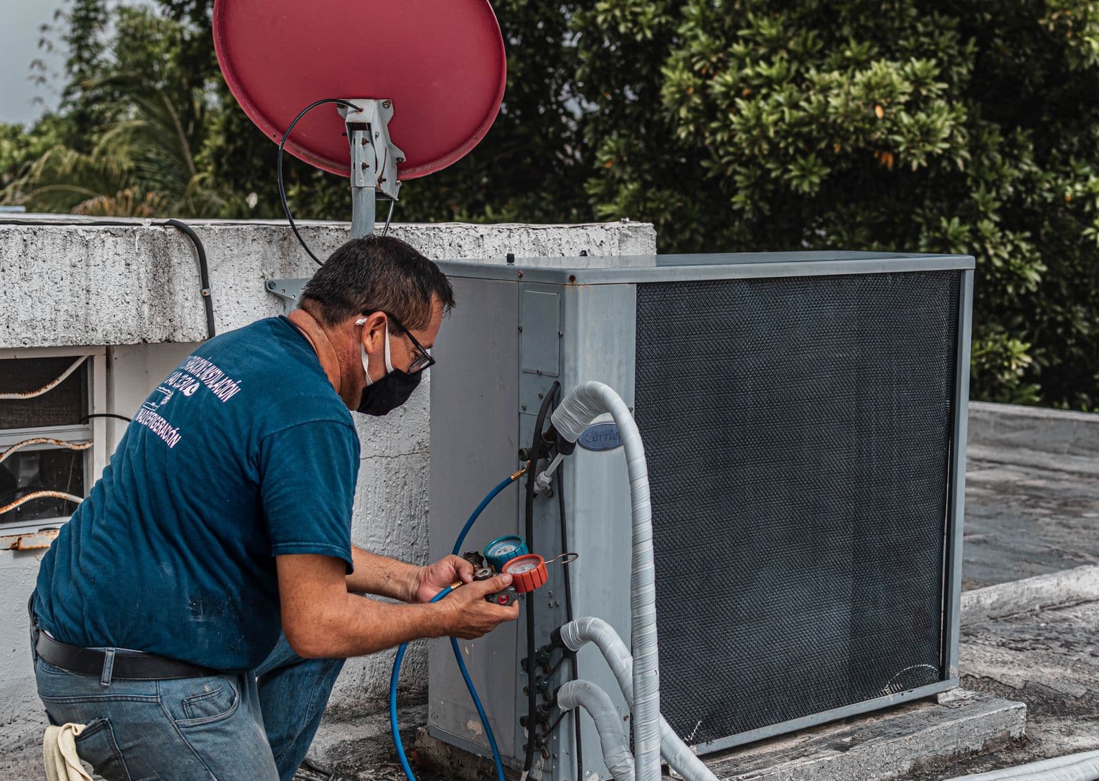 HVAC technician using refrigerant manifold gauges to service a residential AC condenser before summer