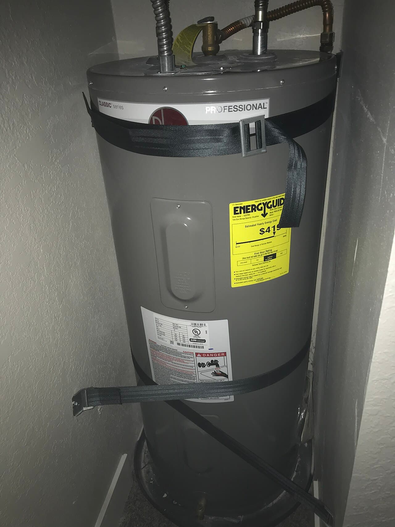 Residential tank water heater installed in a utility closet with copper flex lines and safety straps
